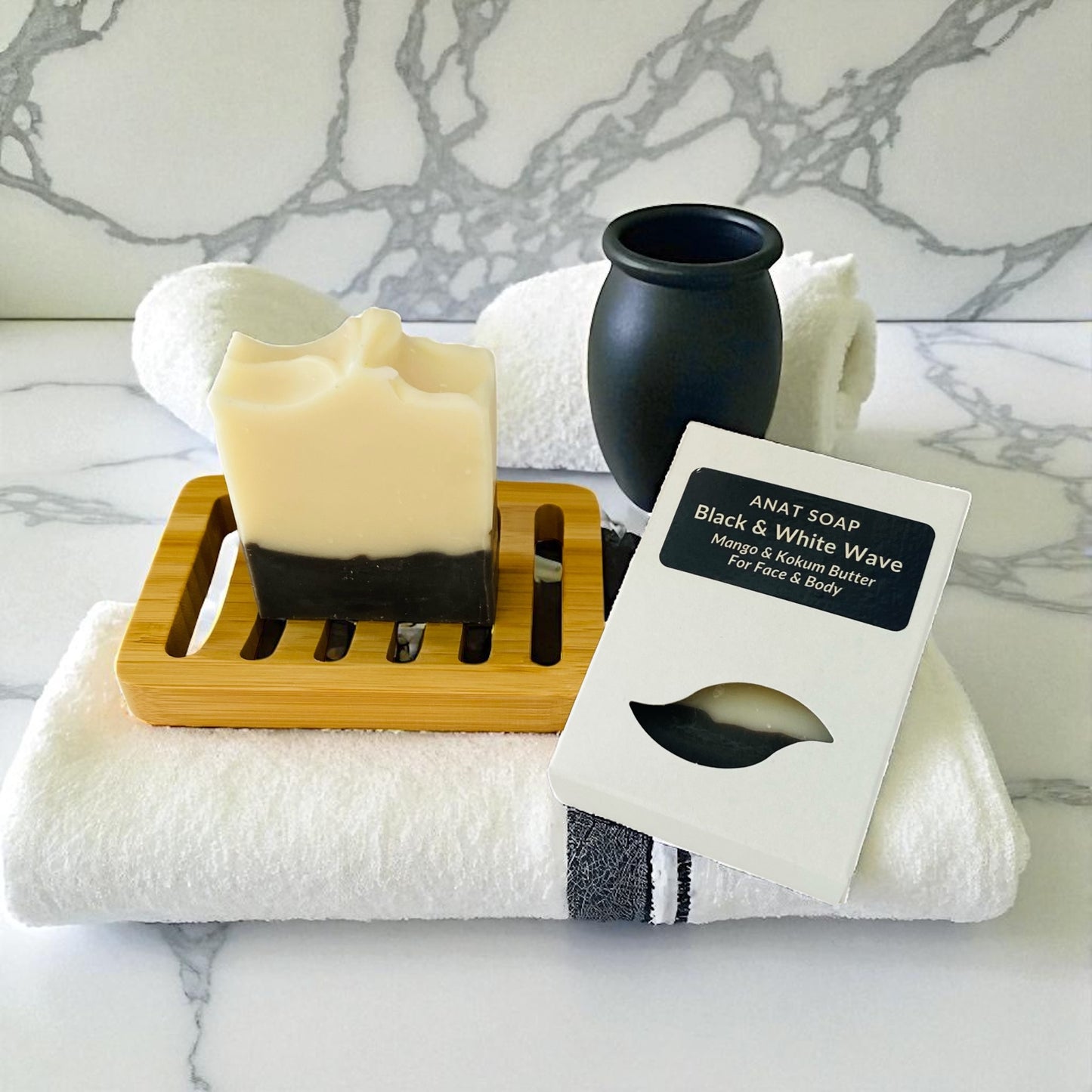 Anat Soap Black & White Wave handmade plant-based soap bar with mango and kokum butter for face and body, shown on a bamboo soap dish next to the product box.