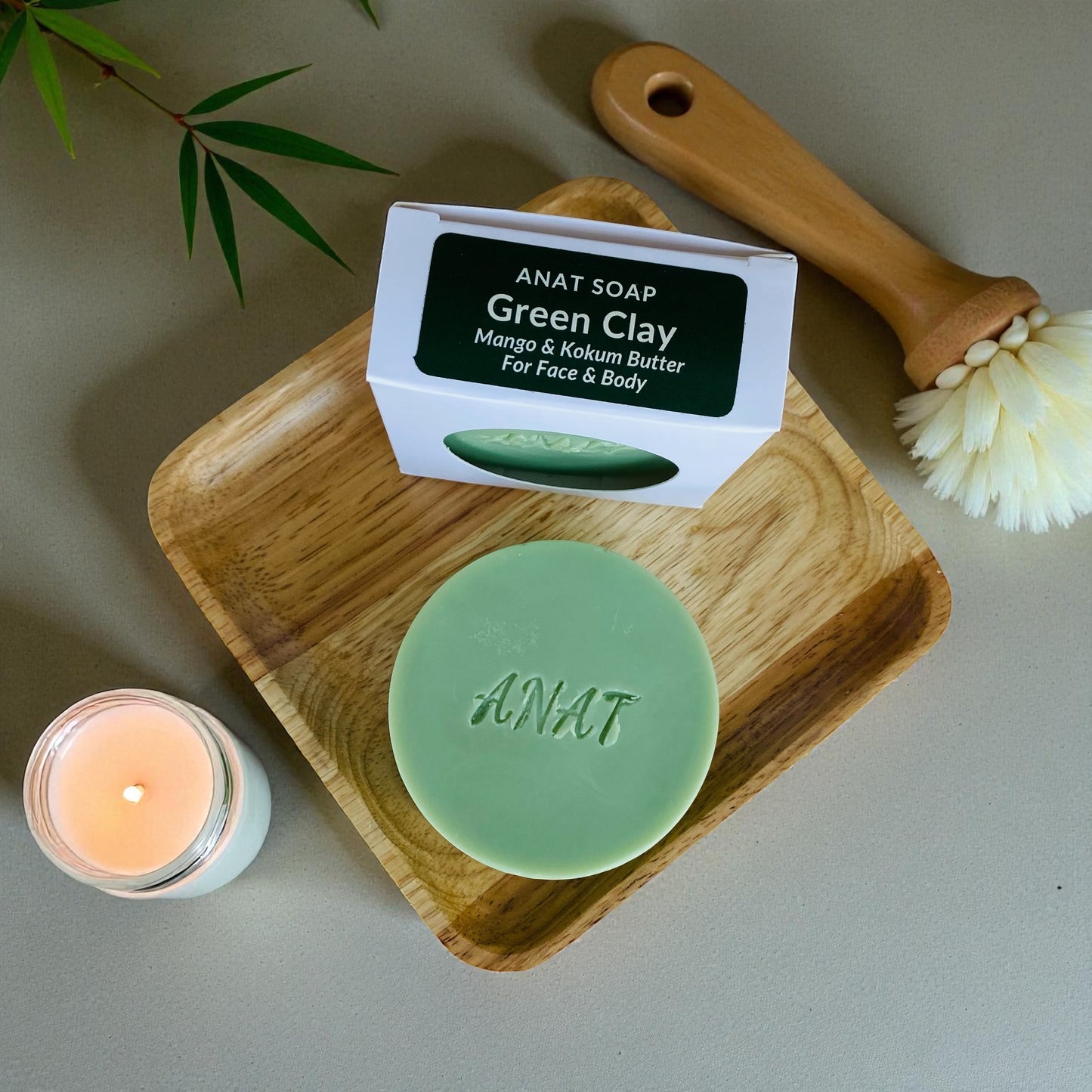Anat Soap Green Clay round handmade plant-based soap bar with mango and kokum butters for face and body, shown on a bamboo soap dish next to the product box.